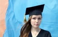 Graduate attractive young girl with red hair dressed in black mantle and square academic before flag Royalty Free Stock Photo