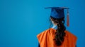 Graduate in cap and gown facing away on blue background, signifying achievement and future opportunities in education