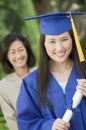 Graduate holding diploma with mother behind outside portrait