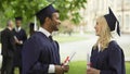 Graduate students with diplomas talking, high-fiving each other, convocation day