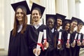 Graduate students standing in a row in black robes with diplomas in their hands outdoor. Royalty Free Stock Photo