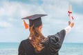 Graduated woman in cap and gown holding certificated celebrating in Commencement day with blue sky on the beach Royalty Free Stock Photo