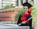 Graduate woman wearing mortarboard and academic dress. Smiling student standing with arms crossed and holding diploma Royalty Free Stock Photo