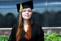 Graduate young girl with red hair dressed in mantle and square academic cap smile in university campus courtyard Royalty Free Stock Photo