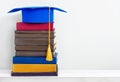 Graduation blue mortarboard on top of stack of books on wooden shelf