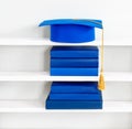 Graduation blue mortarboard on top of stack of books on wooden shelf