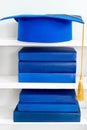 Graduation blue mortarboard on top of stack of books on wooden shelf