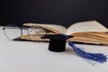 Graduation cap and glasses with open book on a table. Focus on hat Royalty Free Stock Photo