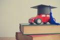 Graduation cap on wooden car over the pile of books on white wall background - Education concept
