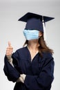 Graduation girl portrait,wearing medical mask. Thumbs up. Self isolation, quarantine, virtual graduation concept