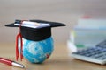 Graduation hat on blue globe with stack of coins money on wooden background, Saving money for education concept