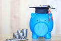 Graduation hat on blue piggy bank with stack of coins money on wooden background, Saving money for education concept Royalty Free Stock Photo