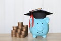 Graduation hat on blue piggy bank with stack of coins money on wooden background, Saving money for education concept Royalty Free Stock Photo