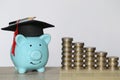 Graduation hat on blue piggy bank with stack of coins money on wooden background, Saving money for education concept Royalty Free Stock Photo
