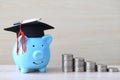 Graduation hat on blue piggy bank with stack of coins money on wooden background, Saving money for education concept Royalty Free Stock Photo