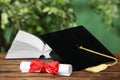 Graduation hat, book and diploma on wooden table against blurred background Royalty Free Stock Photo