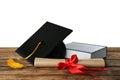 Graduation hat, book and diploma on wooden table against white background Royalty Free Stock Photo