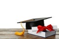 Graduation hat, book and diploma on wooden table against white background Royalty Free Stock Photo