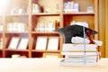 Graduation hat, diploma scroll and books on the table with bookshelf Royalty Free Stock Photo