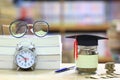 Graduation hat on the glass bottle on bookshelf in the library room background, Saving money for education concept