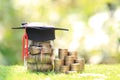 Graduation hat on the glass bottle with Stack of coins money on natural green background, Saving money for education concept