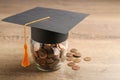 Graduation hat and jar with coins on wooden table. Money saving concept