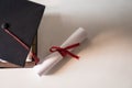 A graduation hat or mortarboard and diploma certificate paper tied with red ribbon on a stack of books with empty space slightly