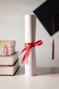 A graduation hat or mortarboard and diploma certificate paper tied with red ribbon on a stack of books with empty space slightly