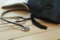 Graduation hat on an open book and a black stethoscope on wooden background