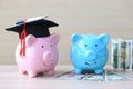 Graduation hat on Pink piggy bank and blue piggy bank with banknote on wooden background, Saving money for education concept Royalty Free Stock Photo