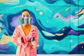 Graffiti female artist painter in respirator mask standing near the wall with her paintings looking to camera Royalty Free Stock Photo