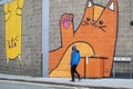 Graffiti of large cats outside of `Kitty CafÃÂ©` in Spaniel Row street with unfocused man with blue coat walking by.
