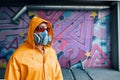 Graffiti painter in respirator mask standing near the wall with his paintings