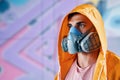 Graffiti painter in respirator mask standing near the wall with his paintings