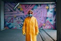 Graffiti painter in respirator mask standing near the wall with his paintings