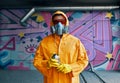 Graffiti painter in respirator mask standing near the wall with his paintings