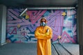 Graffiti painter in respirator mask standing near the wall with his paintings