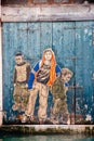 Graffiti portraying three boys on a wooden door of an old building along Venica canals