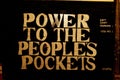 Graffiti style lettering text "Power To The People's Pockets" on the wall