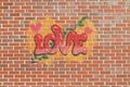 A graffiti of the word love on a background of a wall with bricks. With hearts and leaves and berries.