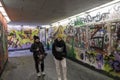 Grafitti wall art in an underpass, two tourists view the writing and designs