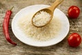 Grain rice in a wooden spoon on a background plates, chili pepper, cherry tomato. Healthy eating, diet, vegetarianism. Royalty Free Stock Photo
