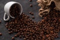 Grains of coffee pour out of a white coffee cup on a dark background from a bag