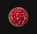 Grains of a pomegranate in woooden bowl isolated on black background. Top view.