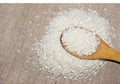 Grains of white rice are a slide in a wooden spoon on an old piece of canvas fabric