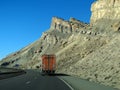 Orange semi truck drives past cliffs