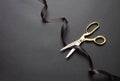 Grand opening. Gold scissors cutting black satin ribbon, black background Royalty Free Stock Photo