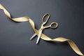 Grand opening. Gold scissors cutting gold satin ribbon, black background Royalty Free Stock Photo