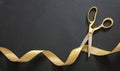 Grand opening. Gold scissors cutting gold satin ribbon, black background Royalty Free Stock Photo