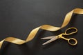 Grand opening. Gold scissors cutting gold satin ribbon, black background Royalty Free Stock Photo